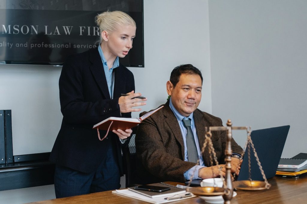 Ethnic male lawyer showing document on laptop to young female colleague